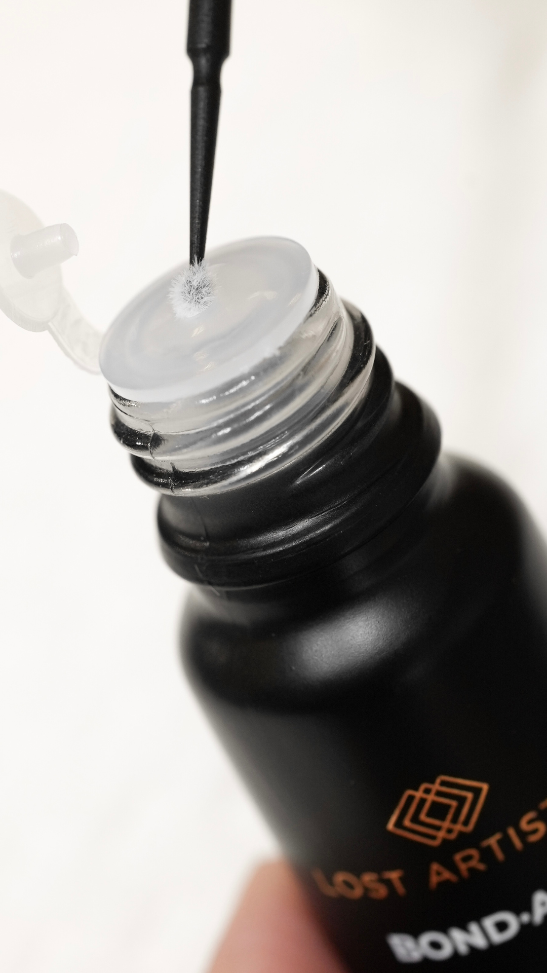 A close up of an open Lost Artistry Bond Aid primer bottle with the applicator brush touching the inner seal, showing the texture of the product.