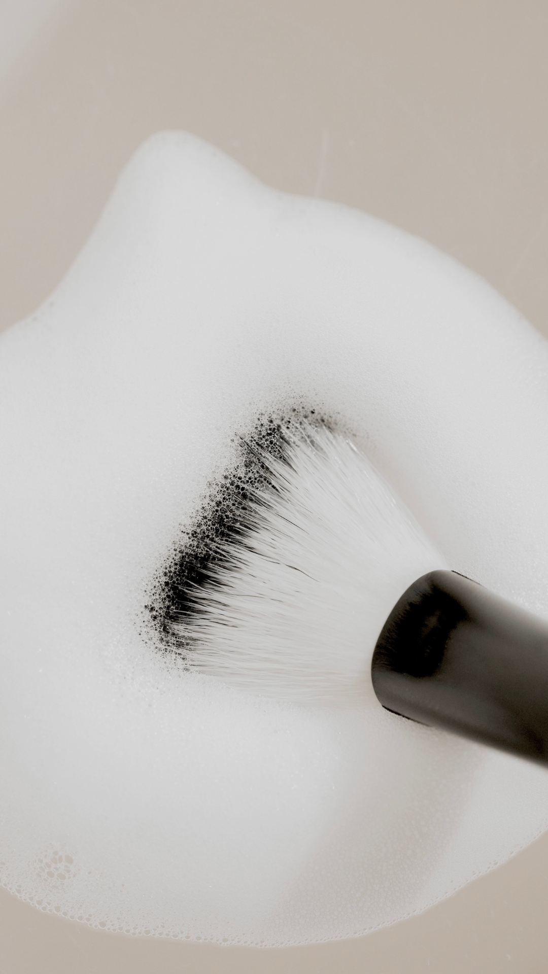 Cleansing brush with black and white bristles resting in a pile of white foam bubbles.