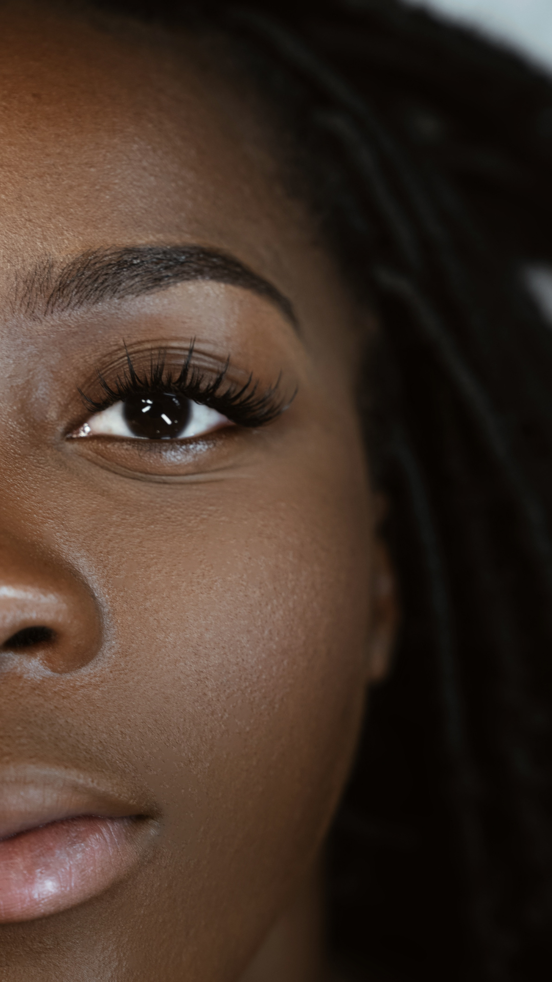 Close-up of a woman’s face showing one eye with long, full eyelash extensions, defined brows, and smooth skin.
