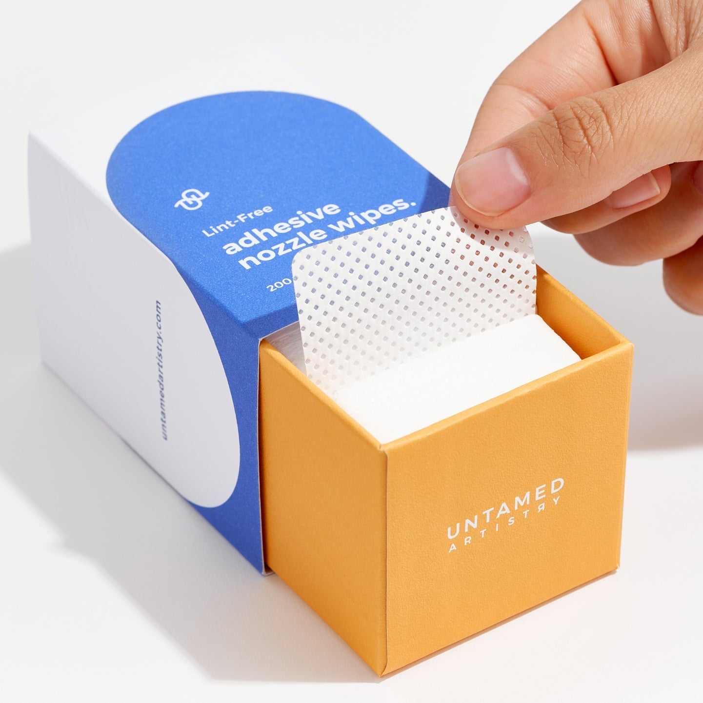 Hand reaching for a white adhesive wipe from an 'Untamed' box on a white background