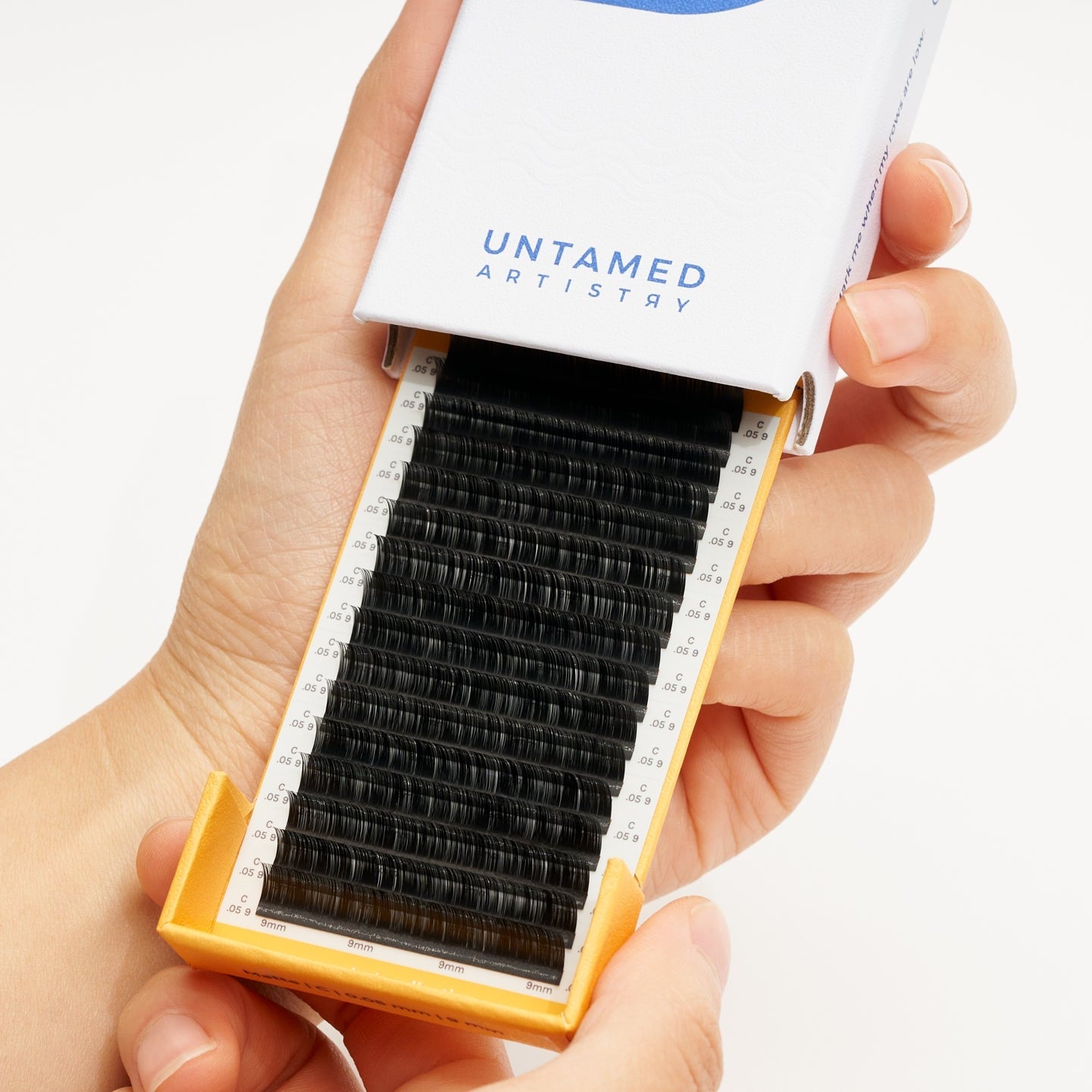 Eyelash extension tray with 'Untamed Artistry' packaging held by a hand on a white background