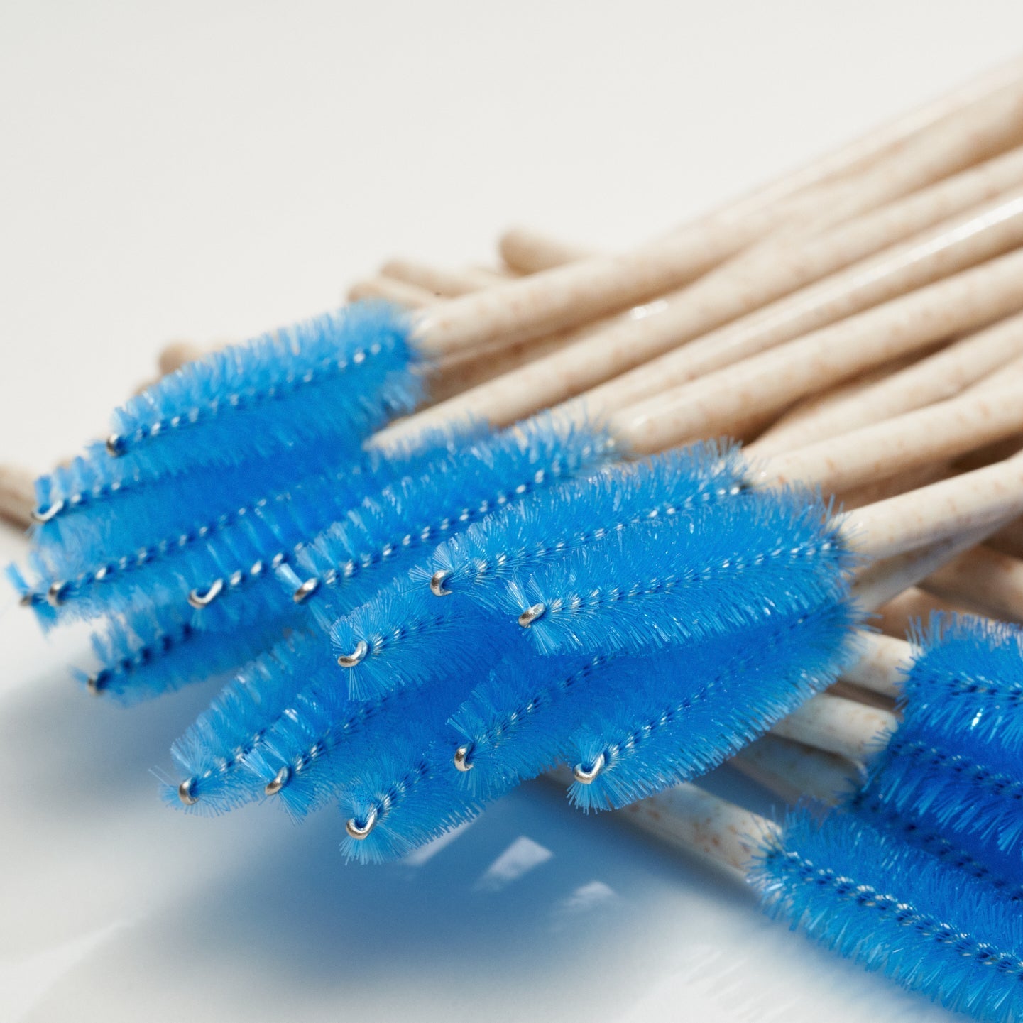 A bundle of small blue bristle cleaning brushes with light wood handles, arranged diagonally on a white background.