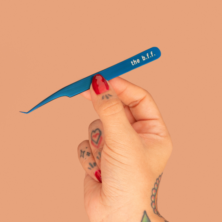Hand holding a blue tweezer with 'the b.t.f.' branding against a beige background