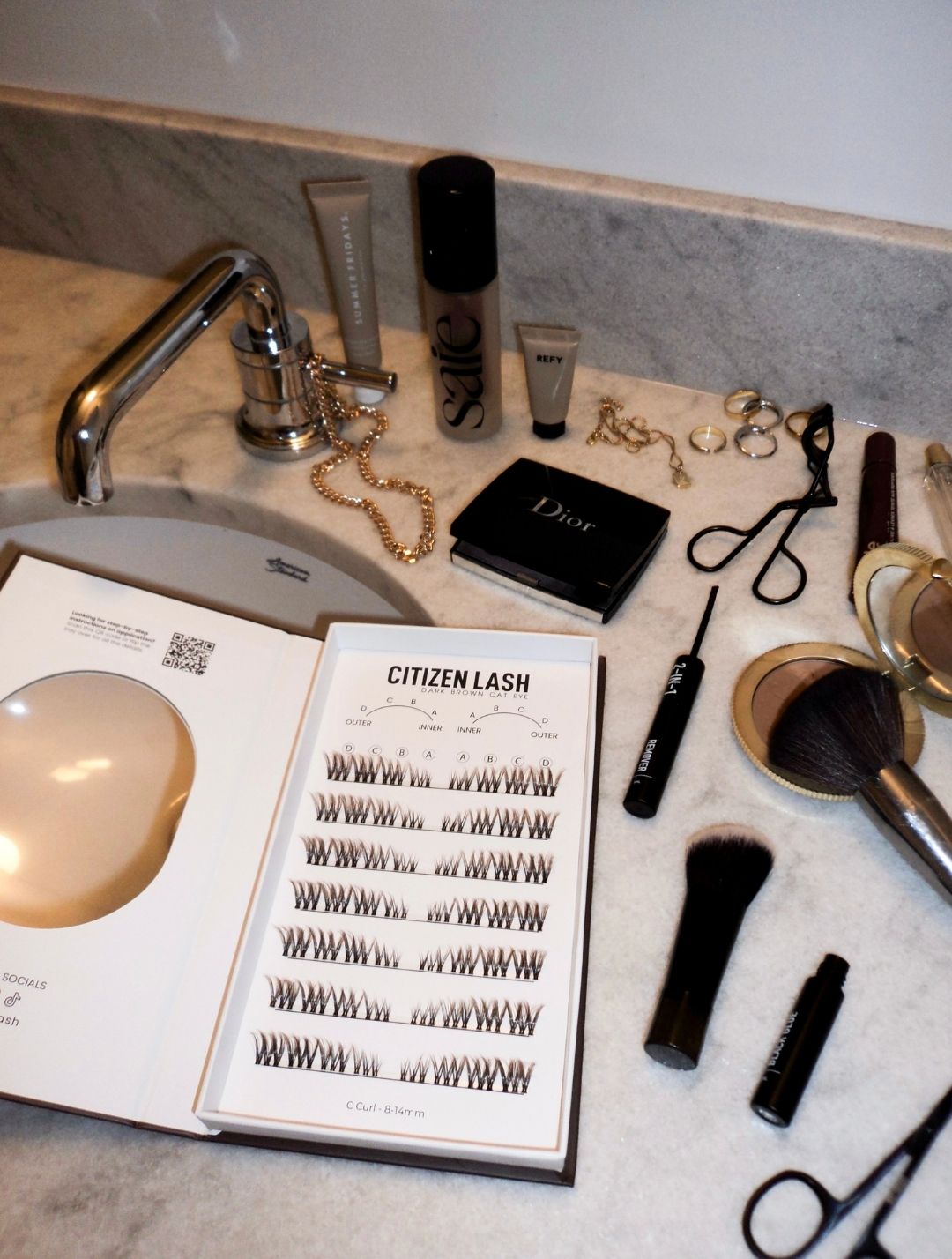 Makeup items and a lash tray on a marble countertop