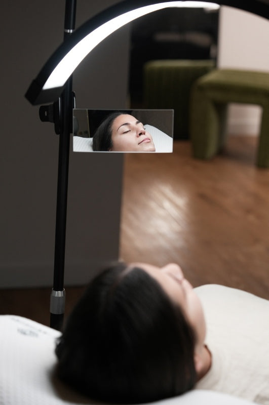 Person lying down with a mirror reflecting their face and a lighted lamp above.