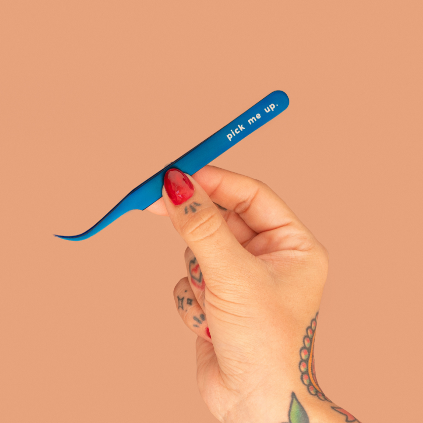 Hand holding a blue tweezers with 'pick me up' text against a beige background