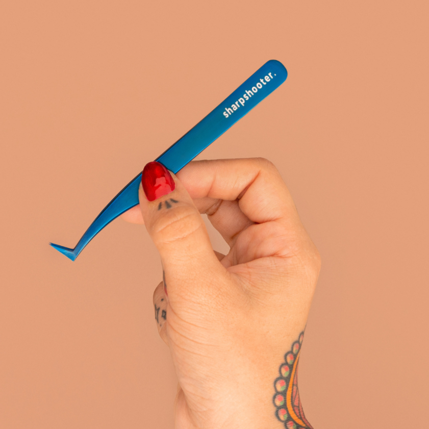 Hand holding a blue tweezer with 'shipshape' branding against a beige background