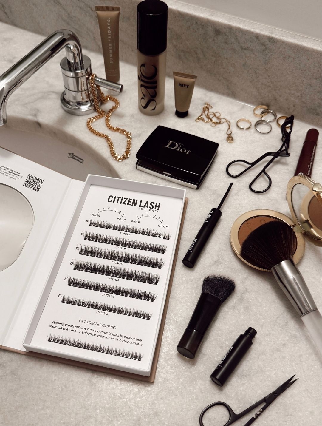Makeup products including eyelash extensions, brushes, and a Dior box on a bathroom counter.