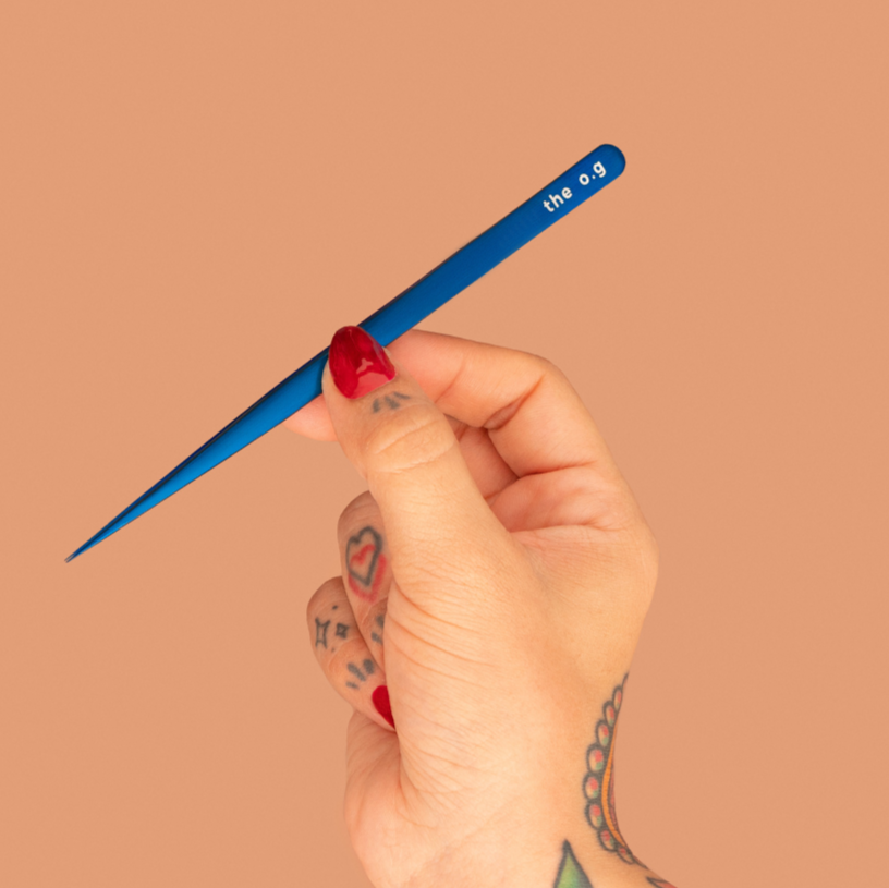 Hand holding a blue makeup brush against a beige background