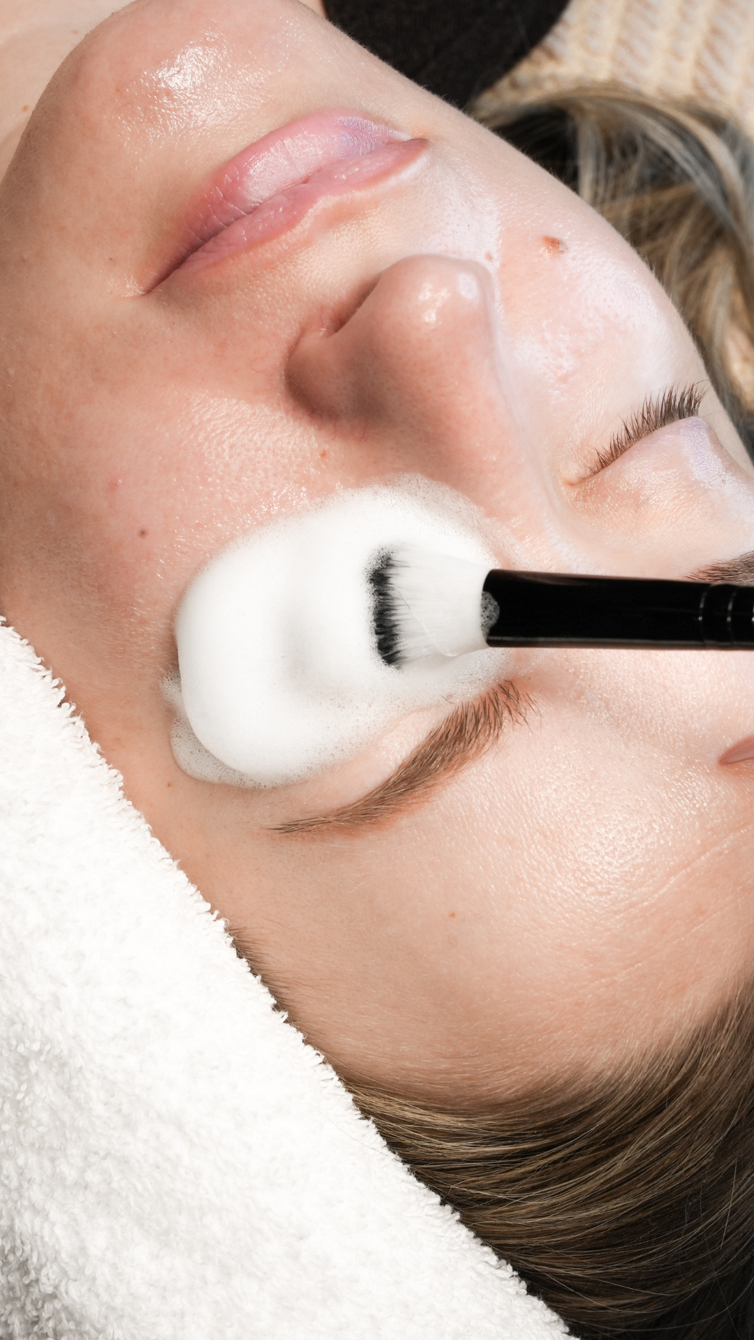 Close-up of a client’s eye area during a lash service, with a cleansing brush applying foam cleanser to the eyelashes.