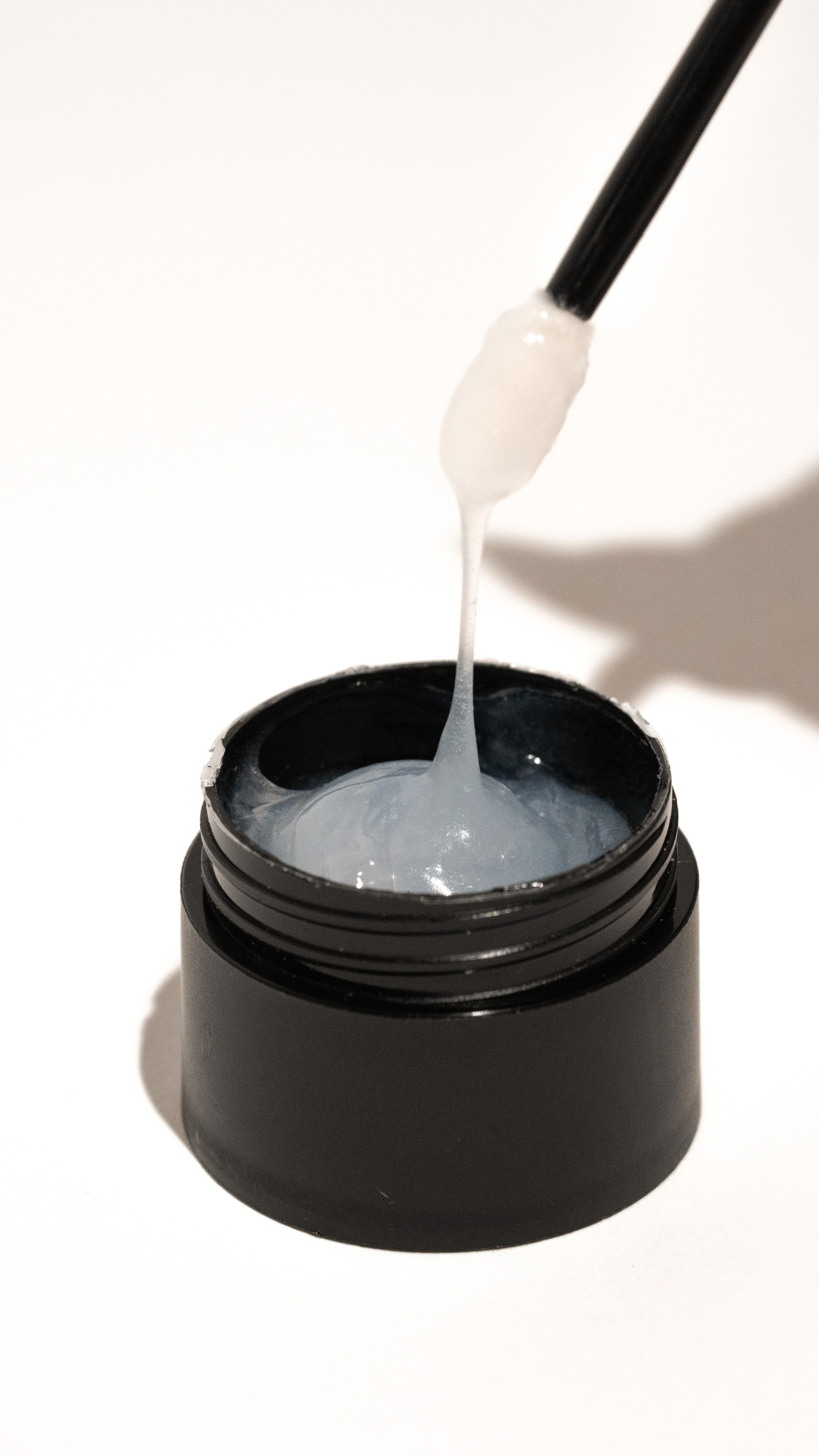 Open black jar of Lost Artistry cream remover with a spatula lifting out thick, white gel-like product.