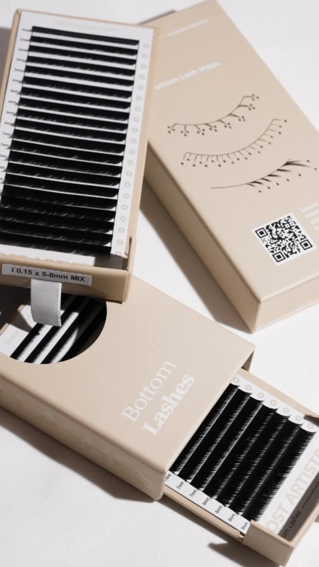 Flat lay of bottom lash extension trays in neutral packaging, showing multiple lash lengths and a beige box labeled bottom lashes.