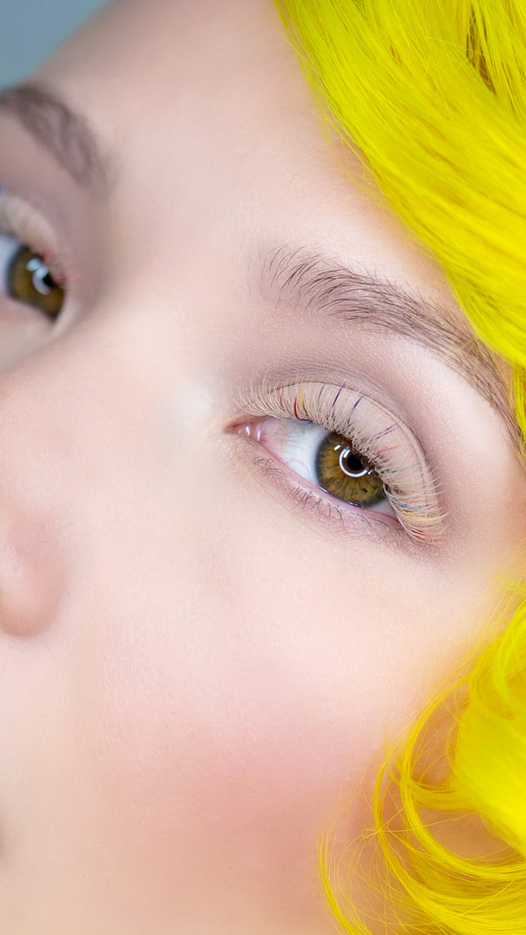 Close-up of a person with bright yellow hair, showing lifted natural lashes with a lash lift treatment.