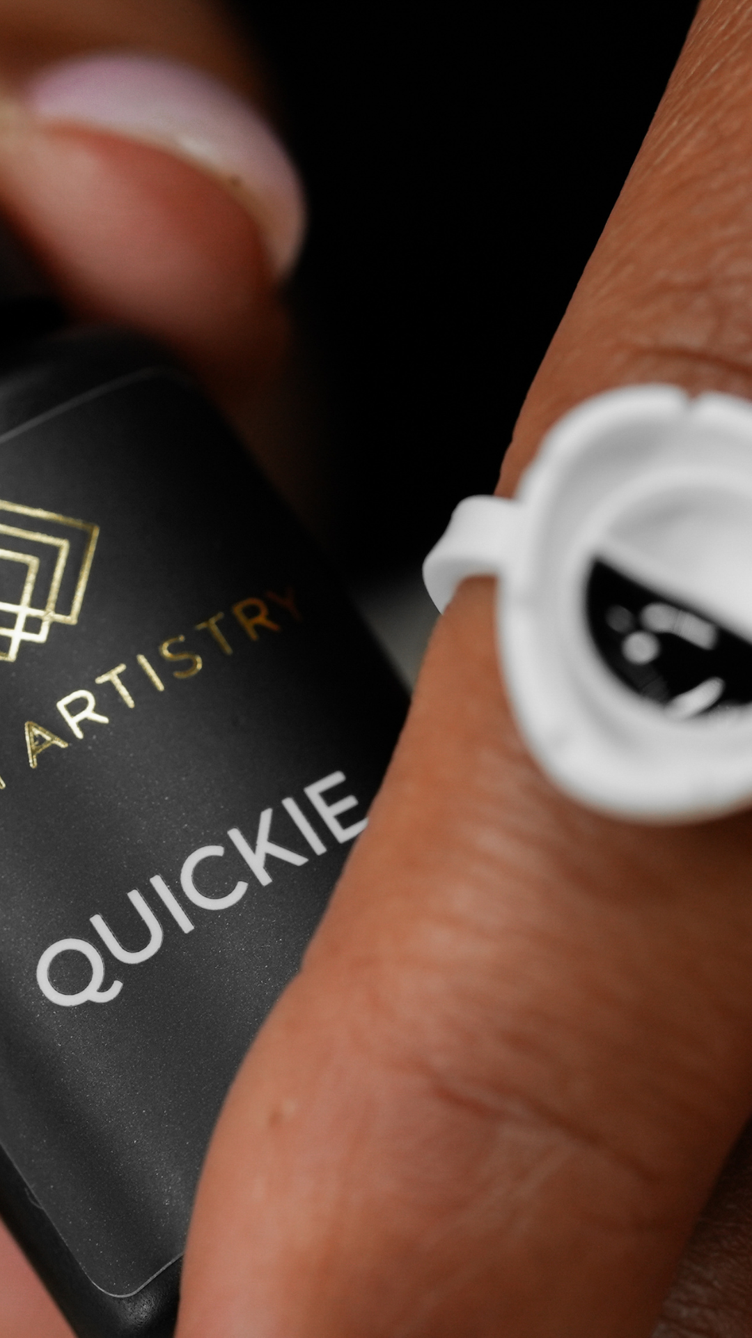 Hand holding Lost Artistry Quickie lash adhesive bottle with the nozzle showing fresh black glue inside.