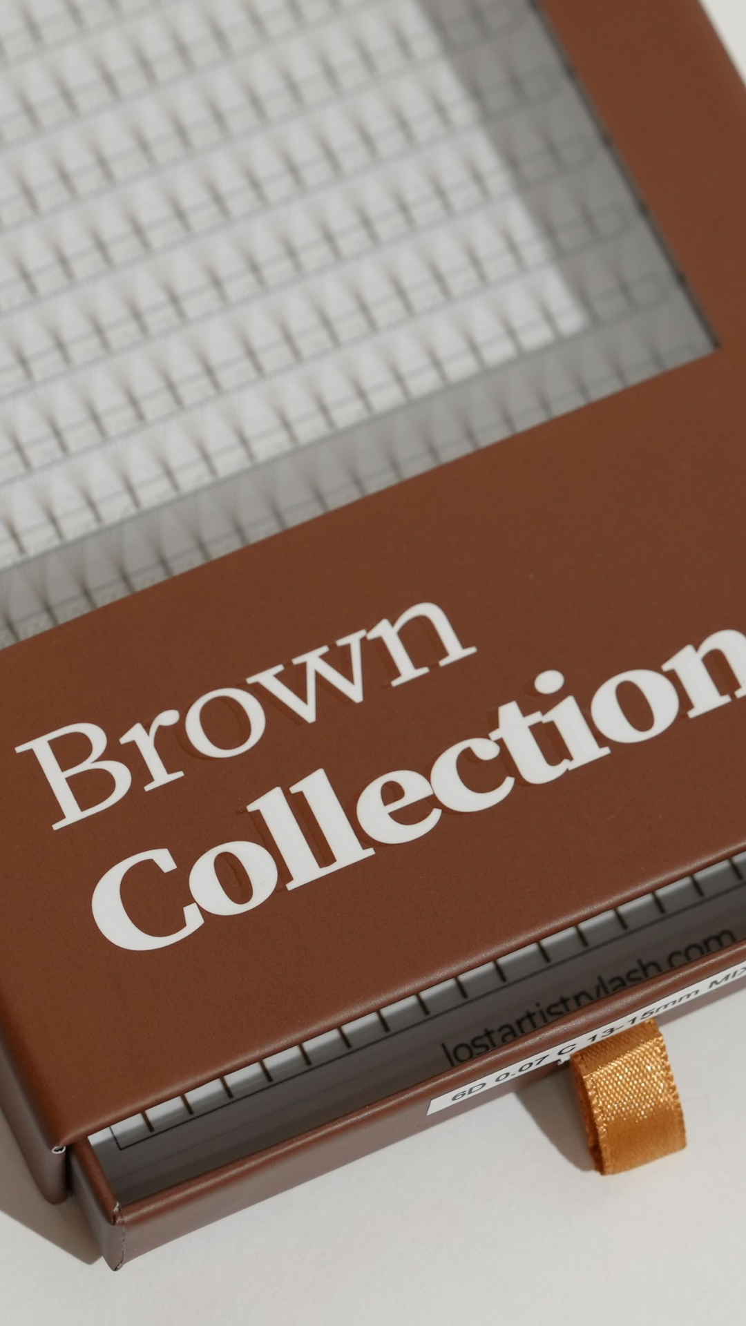 Close-up of a Lost Artistry lash tray from the Brown Collection, showing neatly arranged rows of brown eyelash extensions in the packaging.