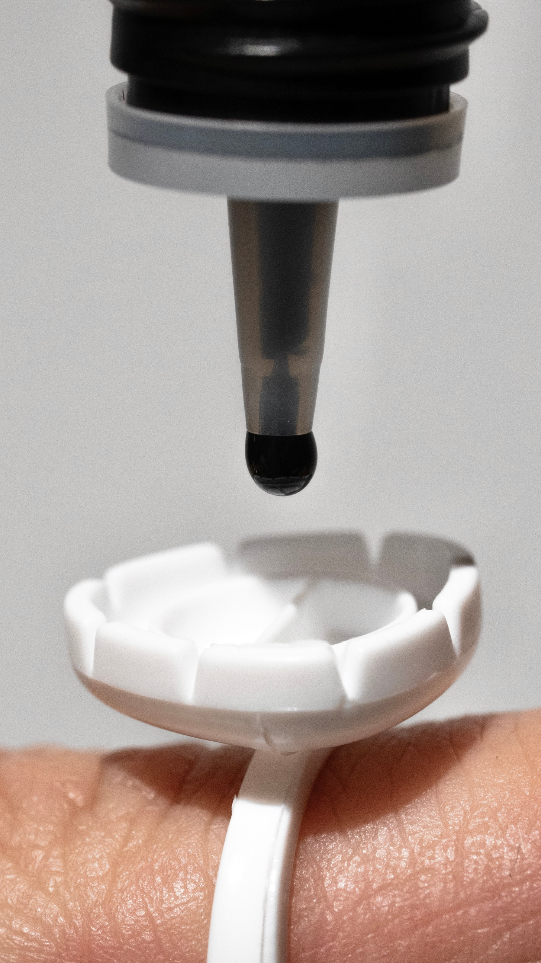 Black lash adhesive dispensing from bottle nozzle into a white glue ring worn on a finger.