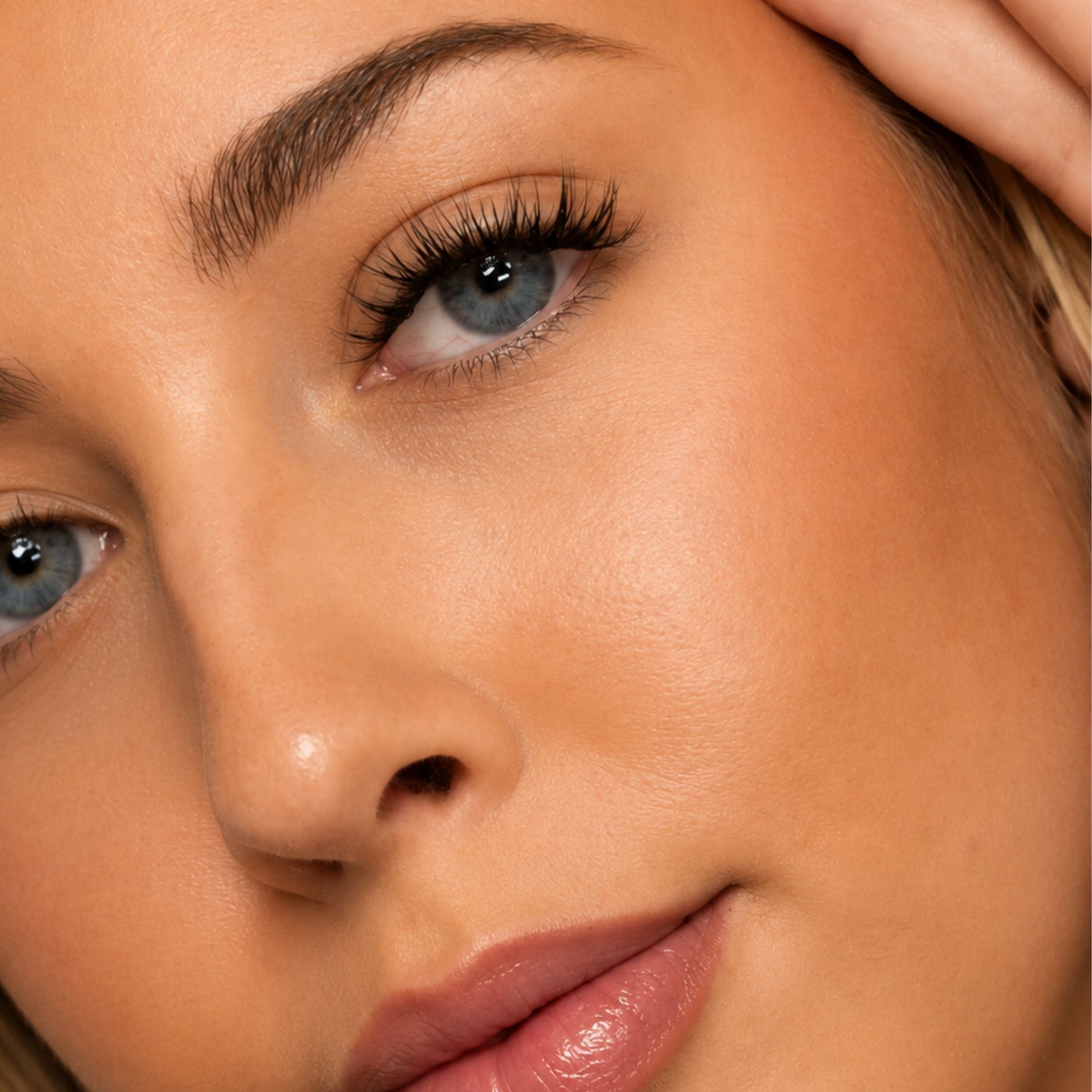 Extreme close-up of a woman's face showing natural skin texture, blue eyes, and makeup on her lips and nose.