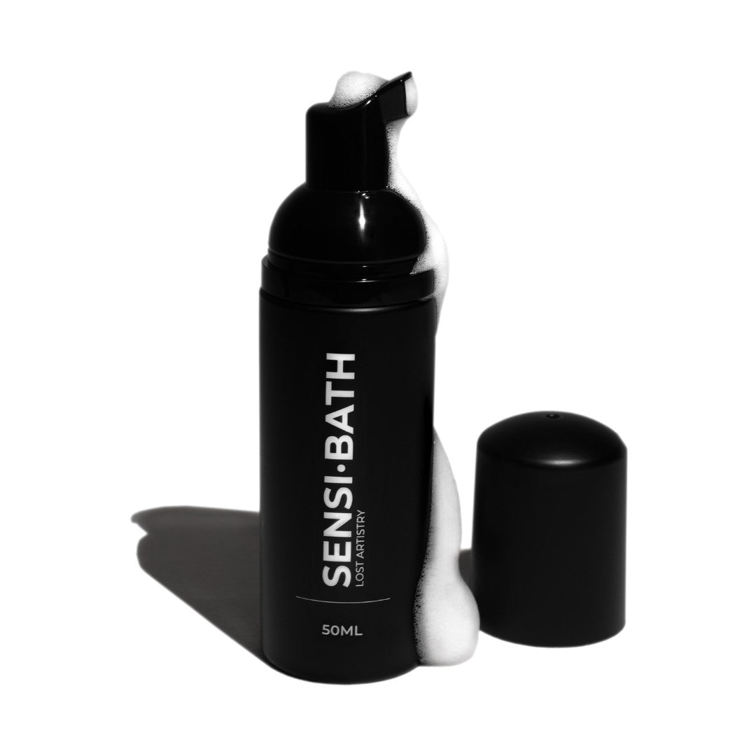 Black bottle of Sensi Bath with pump and white foam on a white background
