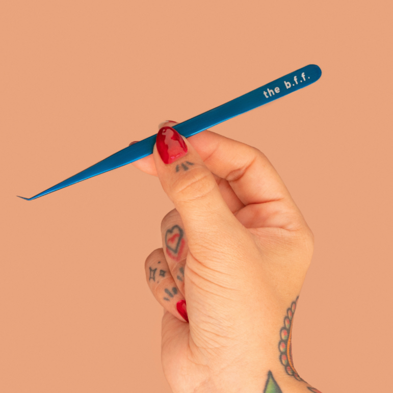 Hand holding a blue makeup tool with 'the b.l.f.' branding against a beige background