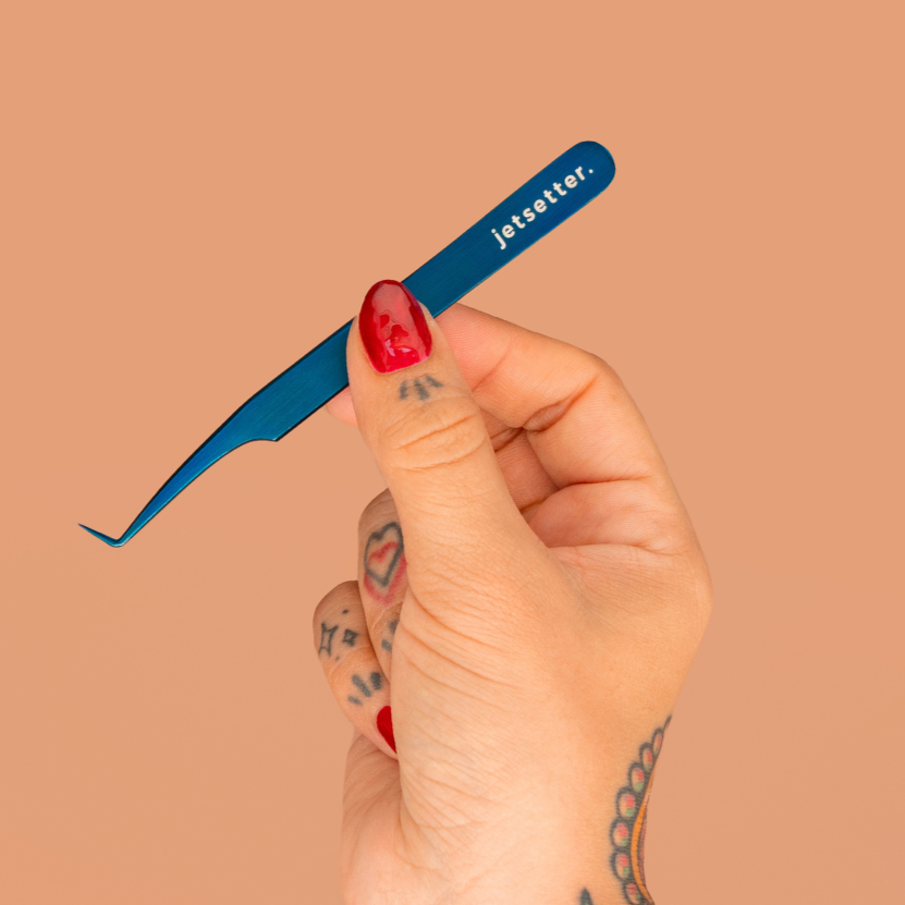 Hand holding a blue tweezer with 'jetsetter' branding against a beige background