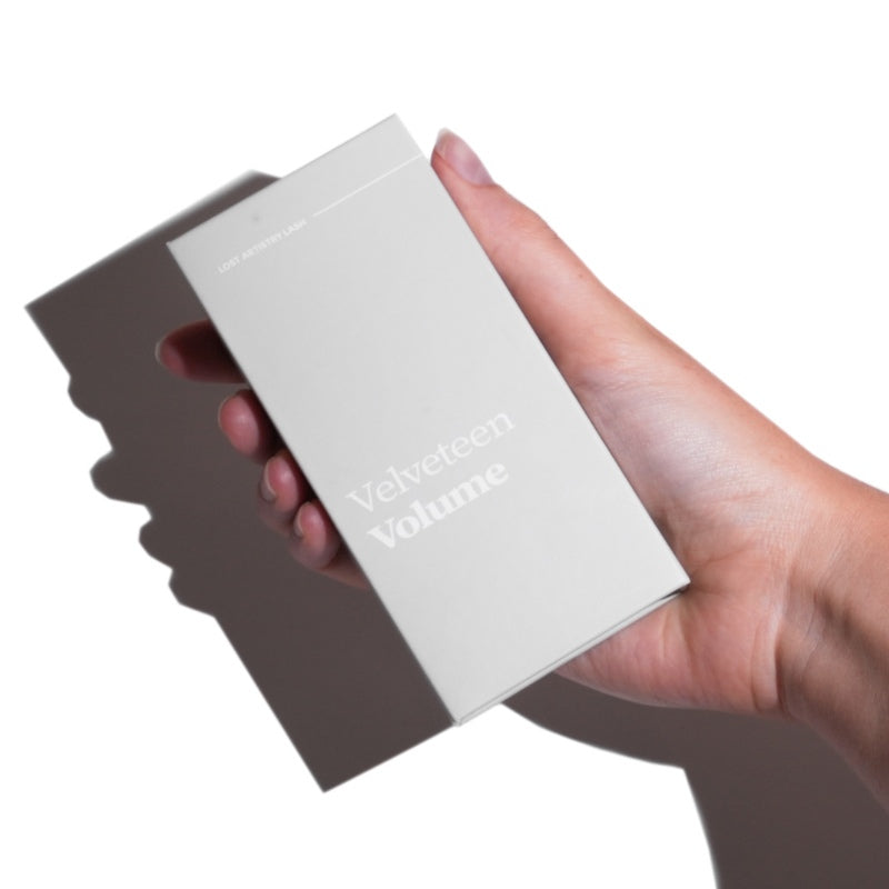 Hand holding a white box with 'Velveteen Volume' text on a white background